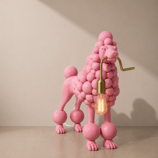 A pink poodle-shaped table lamp with a cluster of glossy pink spheres forming its body, a brass-colored metal arm, and a glowing warm bulb, set against a neutral beige background.